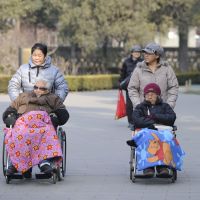 Keeping mobile: Two elderly people are pushed on wheelchairs at a Beijing park Tuesday. Frailty rising as a medical condition