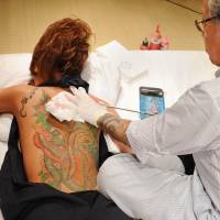 Master at work: Japanese tattooist Horiyoshii III tattoos a flower on the back of a woman. Traditional Japanese tattoos like this can be quite painful but perhaps not as painful as discovering the kanji you had inked on your skin doesn't mean what you thought it did! Best to consult an expert before getting a cryptic <em>kanji</em> tattoo