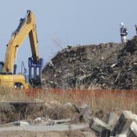 Still standing: A worker stands atop a pile of debris as an excavator operates nearby in Minamisoma, Fukushima Prefecture, on Saturday. The waste was thrown together by the mega-earthquake and tsunami of March 11, 2011. Job seekers and offers in Tohoku still mismatched
