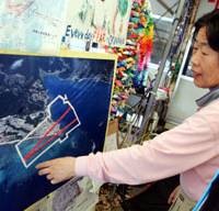 A protester on May 22 points to the spot on an aerial photo of Henoko, northern Okinawa Island, where two runways will be built for the relocation of the U.S. Marine Corps Air Station Futenma. Back to square one after Okinawa poll?