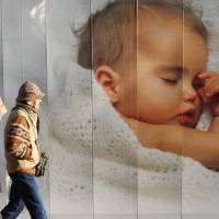 Modern parenting: An elderly couple in Tokyo walk past an advertisement displaying a picture of a baby. Today’s parents pay big money for devices and information in the search for help in putting their little darlings to sleep. An introspection on what's behind the make-your-baby-sleep industry