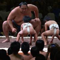 Two on one: A Japanese sumo teacher engages in a mock match with two children during an exhibition before a two-day sumo tournament in Jakarta on Aug. 24. Japanese culture grips Indonesia as firms flood in