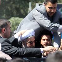 Missed: Bodyguards protect Iranian President Hassan Rouhani (in glasses) after a shoe was thrown at his car in Tehran on Saturday. Iranian protester hurls shoe at Rouhani after phone conversation with Obama