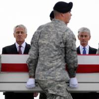 Defense Secretary Chuck Hagel (left) and Army Secretary John McHugh (right) watch as the remains of a soldier killed in Afghanistan are carried at Dover Air Force Base, in Delaware, last Wednesday. Medal of Honor seen as vindication for war hero