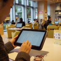 Paperless: A woman reads an e-book via a complimentary tablet computer at honto cafe in Tokyo. The cafe run by Dai Nippon Printing Co. lets people use its reading app. Japan's readers slower to make e-book leap