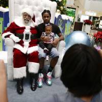 Dreaming of a multicolored Christmas: Dressed as Santa Claus, Langston Patterson (left) poses with Davonte Hager and his daughter Maliyaah, 1, at Baldwin Hills Crenshaw Plaza mall in Los Angeles. Santa Claus has many faces, races