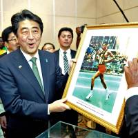 Sports legend: Prime Minister Shinzo Abe holds a photograph of Ethiopian marathon runner Abebe Bikila, presented to him by Bikila's son, in Addis Ababa on Monday. Abe recalls Abebe, meets Ethiopia's running heroes