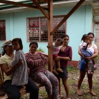 Behind closed doors: Filipinos in the Cebu village of Ibabao accompany their children to a day care center next to the now-abandoned house (rear right) that was used to stream live sex acts of children to pedophiles online overseas. Online child porn ring shocks Cebu