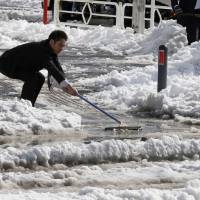 A worker uses a squeegee to push snow from a walkway into a street in Yokohama on Saturday. Frozen ideas slow snow response