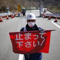 A security worker holds a flag reading “Please Stop!” as he stand by a steel gate marking the border between the towns of Tamura and Okuma in Fukushima Prefecture on Tuesday. Fukushima-linked cancer surge unlikely: U.N.