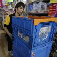 A worker at mass-market retailer Don Quijote pushes crates through aisles full of goods while restocking shelves at an outlet in Tokyo on May 28. Top retailers reach crossroads in labor shortage shakeout