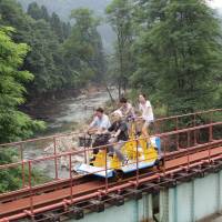 Visitors ride a pedal-driven rail cart over a river at a defunct mine in Kosaka, Akita Prefecture, last August. The area got a tourism boost Sunday with the opening of the Kosaka Railroad Railpark. Abandoned railway reborn as theme park