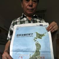A man poses Wednesday in Chongqing, China, with a full page map with the headline “Japan wants a war again” and showing mushroom clouds over Hiroshima and Nagasaki that was published in the July 3 issue of the Chongqing Youth Daily newspaper, days after Japan reinterpreted its war-renouncing Constitution to allow a greater military role. Japan protests China paper's map of atomic clouds