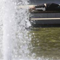 Weather extremes: A man lies in the sun near a water fountain on Aug. 6. Weather systems stalling more often