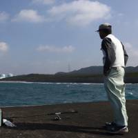 A fisherman gazes at the two reactors of Kyushu Electric Power Co.'s Sendai nuclear plant in Satsumasendai, Kagoshima Prefecture, on Monday. Town divided after Sendai nuclear plant restart clears another hurdle