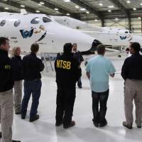 National Transportation Safety Board investigators stand Sunday near the WhiteKnightTwo in Virgin Galactic's hangar in Mojave, California. The cause of Friday's crash of Virgin Galactic's SpaceShipTwo has not been determined, but investigators found the feathering system, which rotates the tail to create drag, was activated before the craft reached the appropriate speed, NTSB Acting Chairman Christopher Hart said. Rocket plane's tail activated prematurely in fatal crash