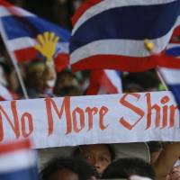 Anti-government protesters wave a banner and Thai national flags as they rally outside the government complex in Bangkok on Wednesday. Impeachment process begins for ousted Thai PM Yingluck