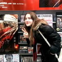 Child’s play: Artist Reylia Slaby stands in front of a display of Mr. Children’s new single, “Ashioto — Be Strong,” in Osaka. Slaby designed the artwork for the release. U.S. artist gets a major photo opportunity from Mr. Children