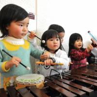 Children play with a xylophone in the music lobby of Kodomo-no-shiro in Tokyo’s Shibuya Ward last Friday, ahead of the facility’s closure. Below, young patrons and their parents listen to a music teacher inside the complex. Venerable Children's Castle in Tokyo set to close after 30 years