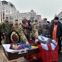 A serviceman places carnations on a coffin Thursday in central Kiev during the funeral ceremony of Kirill Geintz, a 28-year-old Russian who was killed while fighting with the Ukrainian volunteer battalion of Santa Maria. Russia's tactics in Ukraine could inspire China, Iran: study