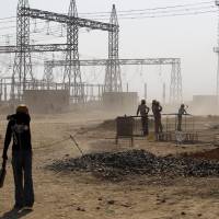A worker shields himself from dust at a coal-fired power plant in Kudgi, India, being built with climate funding from the Japan Bank for International Cooperation, on Feb. 24. JBIC agreed in January 2014 to provide $210 million in loans to Indian utility NTPC Ltd. to buy equipment from a local Toshiba Corp. subsidiary. Japan accused of financing coal-fired power plants