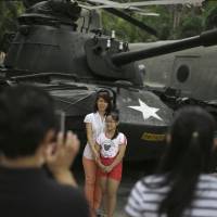 Visitors have their photos taken near a tank used by the U.S. Army during the Vietnam War at the War Remnants Museum in Ho Chi Minh City on Wednesday, ahead of 40th anniversary celebrations Thursday of the end of the conflict. On the green, Vietnam army's capitalist streak
