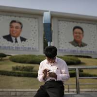 A man using a smartphone sits in front of portraits of late North Korean leaders Kim Il Sung and Kim Jong Il in Pyongyang on Tuesday. With caveats, online shopping site makes debut in isolated North Korea