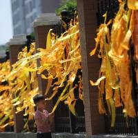 A boy touches a yellow ribbon tied on a fence for passengers of the capsized cruise ship, outside Yusha primary school in Jianli, Hubei province, China, on Saturday. Once obscure Chinese town rallies after ship disaster