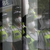 Police officers wearing masks as a precaution against infection are reflected on windows in Seoul on Tuesday. South Korean hospitals suspend services as MERS outbreak spreads