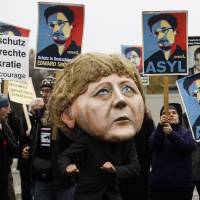 A demonstrator with a mask depicting German Chancellor Angela Merkel poses in front of other protesters holding posters of former National Security Agency contractor Edward Snowden outside the German parliament building in Berlin in November 2013. German spy chief thanks Snowden for raising counter-espionage awareness