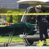 A worker wheels a gurney with a body bag on it, under the green cover, to a coroner’s van outside of a home in Broken Arrow, Oklahoma, Thursday, where five family members were discovered stabbed to death. Two male teenagers are in custody. Police say they and the victims are related. Five in Oklahoma family found fatally stabbed; siblings caught in nearby woods