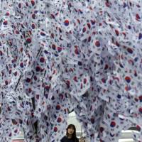 A woman looks at South Korean national flags hanging on trees in downtown Seoul on Aug. 13 ahead of the 70th anniversary of Independence Day on Saturday. Lotte faces backlash in South Korea over ties to Japan