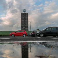 Automobiles sit in a parking lot as the VW logo sits on top of a building under construction at the Volkswagen AG headquarters in Wolfsburg, Germany, on Wednesday. Sell, sue or stay put: considerations for Volkswagen owners