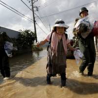 Yoshiko Nakamura, 66, is escorted Saturday by Self-Defense Force’s soldiers as she leaves her home in Joso, Ibaraki Prefecture, where the torrential rains of Typhoon Etau caused major flooding last week. Stores fire up their networks to quickly send aid to flood areas