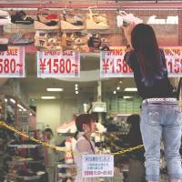 A worker places a shoe on a display as a footwear store prepares to open in Tokyo’s fashionable Harajuku district. Retailers warn of dismal spending; sales tax hike seen stifling demand