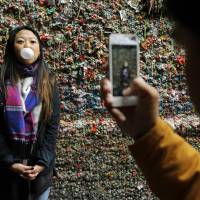 Jessica Wang, visiting from Los Angeles, has her photo taken by Michael Teylan at Seattle’s “gum wall” at Pike Place Market, Monday. Steam targets Seattle market's famed 'gum wall' after 20-year accumulation