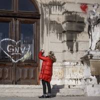 A woman snaps a picture outside the Grand Theatre de Geneve in Geneva on Sunday after vandals painted graffiti on its wall during a demonstration on Saturday night before. Protesters trash parts of downtown Geneva during demonstration against budget cuts