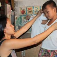 Kean Geronimo, a 7-year-old elementary school boy with a heart defect, puts on a shirt with his mother's help at their home in Manila. Foundation helps poor Philippine kids go to school