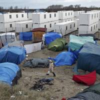 A migrant walks among tents in a makeshift camp as containers are put into place to house several hundred migrants living in what is known as the “Jungle,” a squalid sprawling camp in Calais, northern France, Monday. Bed-equipped shipping containers set to boost soggy Calais 'jungle' camp migrants' lot