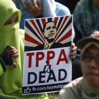 A Malaysian protester poses for a photograph holding an anti-Trans-Pacific Partnership agreement placard with U.S. President Barack Obama’s caricature during a protest in Kuala Lumpur on Saturday. Protesters hit the streets to oppose Malaysia signing TPP