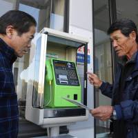 Hiroshi Suzuki (left) checks the procedure to collect coins from a pay phone set up at an emergency meeting point in Tahara, Aichi Prefecture. Aichi Prefecture city rolls out new pay phones in disaster-prevention move