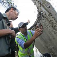 A Malaysian official takes pictures Monday of a piece debris found by fishermen on a beach in the southern Thai province of Nakhon Si Thammarat. Metal on Thai beach not from missing plane; Mitsubishi says it's likely from rocket