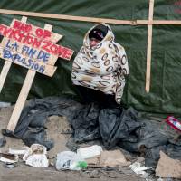 A man sits next to a placard in the northern part of the Jungle migrant camp in Calais, northern France, during the end of the dismatling of the camp's southern part, on Wednesday. France's first international-standard refugee camp opened in northern France on March 7 destined to shelter migrants and refugees living in dire conditions in nearby makeshift camps as they attempt to reach the United Kingdom. Calais migrant slum 'Jungle' nearly cleared; on-site venue urged for hundreds of unsupervised kids
