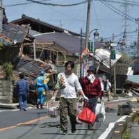 Residents walk on a street next to houses destroyed in the recent earthquakes in Mashiki, Kumamoto Prefecture. on April 17, 2016. Quake-hit areas in Kumamoto give green light to volunteers
