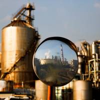 A factory is reflected in a traffic mirror at the Keihin industrial zone in Kawasaki, Kanagawa Prefecture, in November. Japan's economy improved in April, but deflation persists