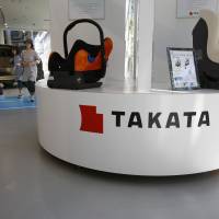 Visitors walk pass by child seats manufactured and displayed by Takata Corp. at an automaker's showroom in Tokyo on May 4. Once projected to be in the black, Takata now sees red as massive recall costs mount