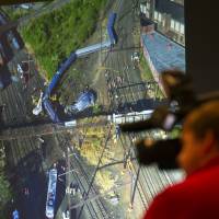 A photograph is displayed on a video monitor of the derailment of Amtrak passenger train in Philadelphia last year during a National Transportation Safety Board (NTSB) meeting on the derailment Tuesday in Washington. NTSB: Amtrak driver distracted by other train's 'rocked' alert, lack of long-sought safety gear led to fatal crash