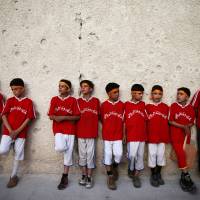 Boys stand by a bullet-riddled wall during a final soccer game in a school championship, in the rebel-held besieged town of Douma, eastern Damascus suburb of Ghouta, Saturday. In show of normalcy, Syria lets students leave besieged areas to take finals