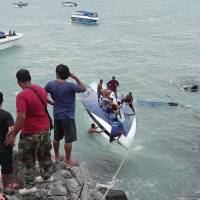 Rescue workers seen in this photo taken from video attempt to retrieve a woman from under a capsized boat of Koh Samui, Thailand on Thursday. Officials say a speed boat carrying 32 tourists and four crew members to the tourist resort island capsized, leaving two foreigners dead and two others missing. Thai rescuers battle rough seas in search for missing British tourist