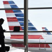 A passenger talks on the phone in January as American Airlines jets sit parked at their gates at Washington's Ronald Reagan National Airport. American Airlines is giving more details on changes that will reward the highest-paying passengers, not just those who fly the most miles, announcing Monday that beginning Aug. 1, passengers will earn points based on the price of their ticket. American joins U.S. rivals, bases frequent flier awards on money spent, not miles flown